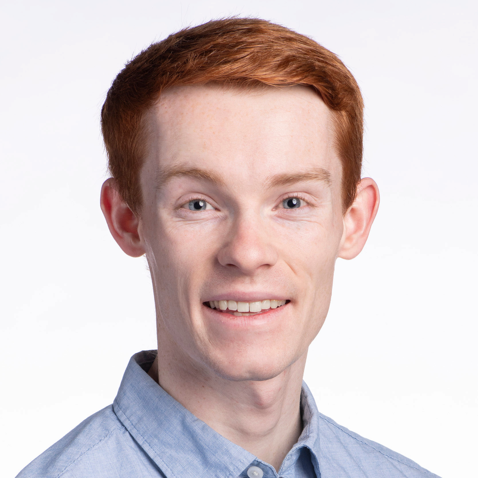 A person smiles toward the viewer in a blue shirt, before a white background.