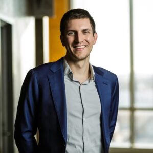 A person in a suit smiles in a sunlit room